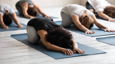 Afrikalı etnik kadın ve ortakları Balasana antrenmanı yapan paspasların üzerinde yatıyorlar