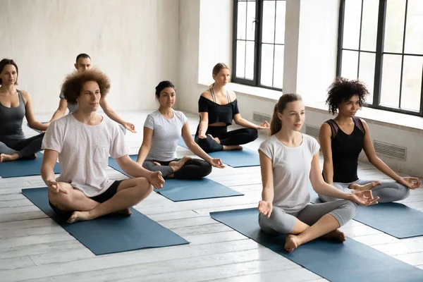 Diverse guys girls sitting in lotus position enjoy meditation process