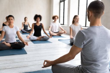 Arka görüş yoga eğitmeni ve içeride meditasyon yapan bir grup insan.