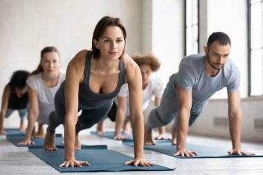 Kadın antrenör ve bir grup insan birlikte tahta pozu veriyorlar.