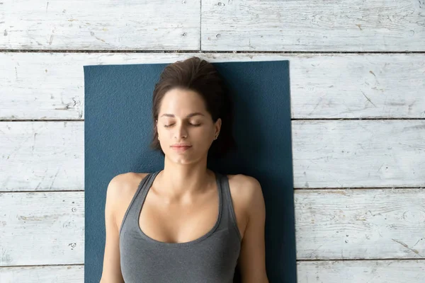 Yukarıda Shavasana pozu sırasında mindere uzanmış genç bir kadın var.