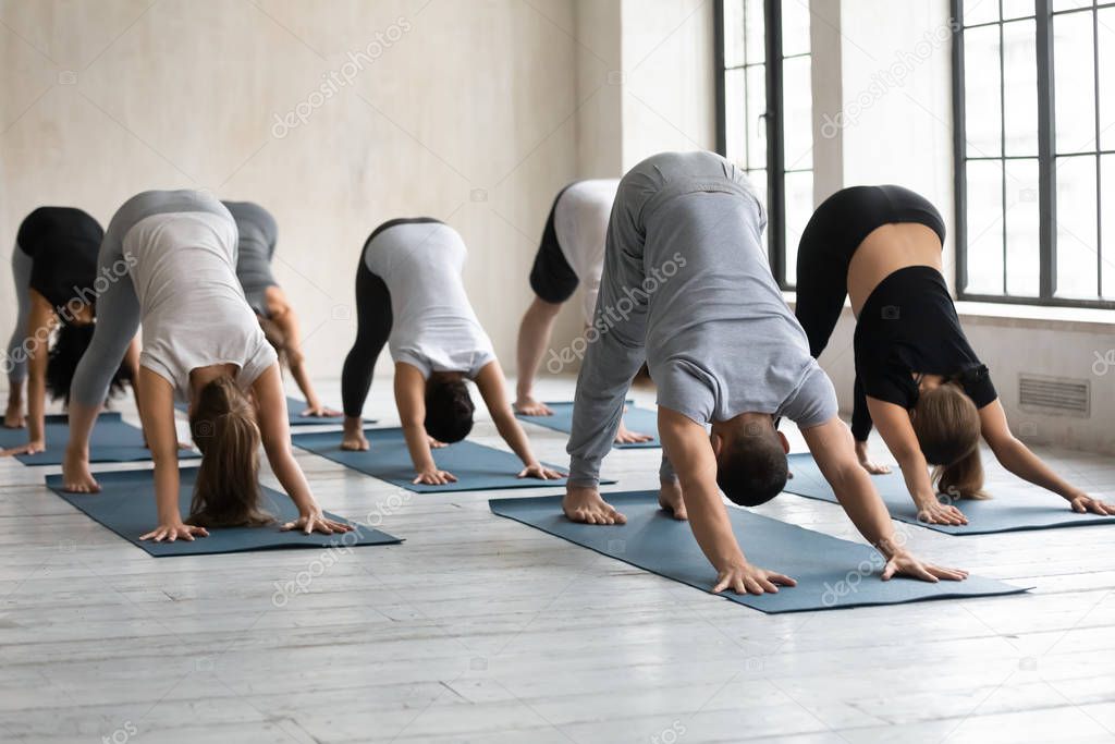 Male coach and group of people performing Downward-facing Dog
