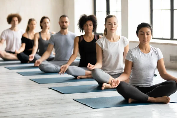 Personas multiétnicas meditando sentadas en posición de loto durante la sesión de yoga — Foto de Stock