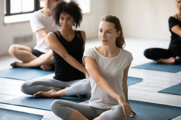 Grupp människor som gör Easy Pose med Twist yoga inomhus — Stockfoto