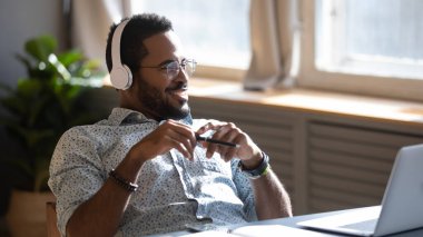 Distracted from job study happy biracial man listening to music.