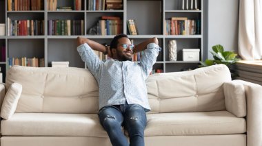 Peaceful young african american man stretching back, relaxing on couch.