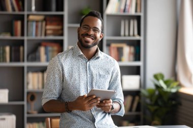 Smiling young biracial man in glasses holding digital computer tablet.