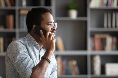 Pleasant handsome biracial man in glasses talking on phone.