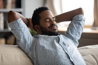 Peaceful carefree biracial guy alone napping on couch indoors. clipart
