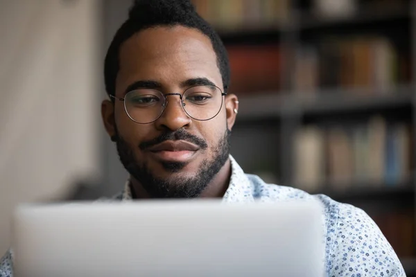 Primer plano enfocado joven africano etnia hombre trabajando en la computadora . — Foto de Stock