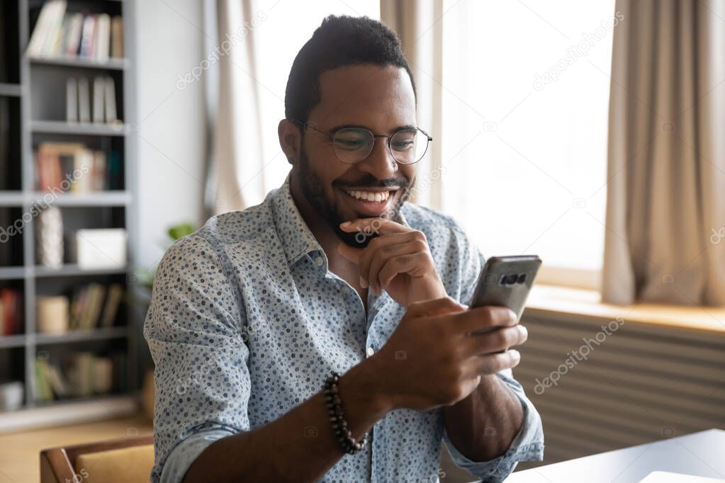 Smiling millennial biracial guy reading pleasant good news sms.