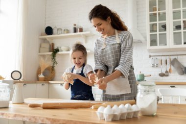 Mutlu anne ve küçük kız mutfakta birlikte yemek pişiriyorlar.