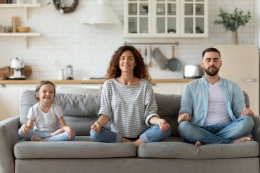 Küçük kızı olan genç bir aile birlikte yoga yapıyor.