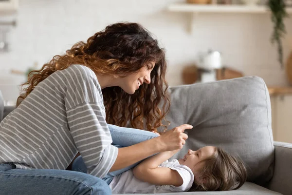 Joven madre jugar con su hija pequeña en el sofá — Foto de Stock