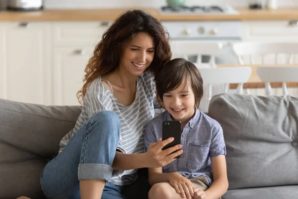 Happy mom have fun using smartphone with little son