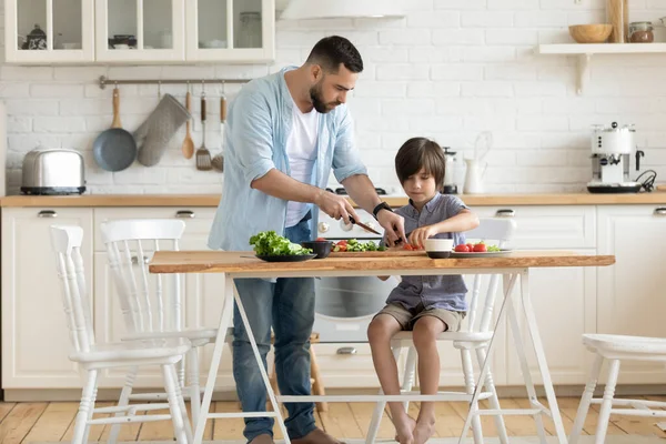 若いお父さんと小さな息子料理一緒にホームキッチンで — ストック写真