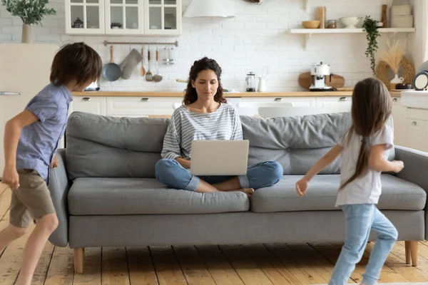 Calma jovem mãe trabalho no laptop sentado com as crianças — Fotografia de Stock