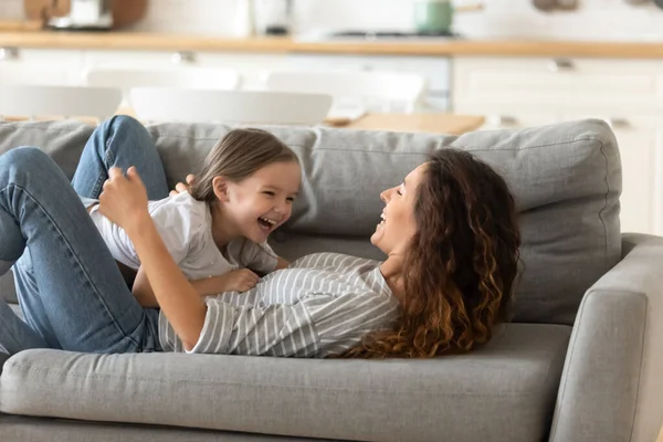 Счастливая мама и маленькая дочь играют на диване — стоковое фото