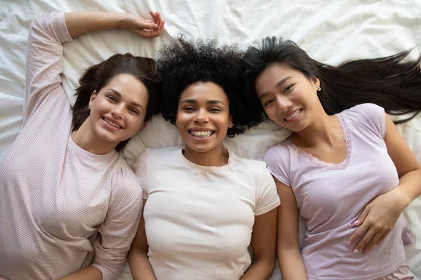 Top view three diverse girls best friends lying on bed — Stockfoto