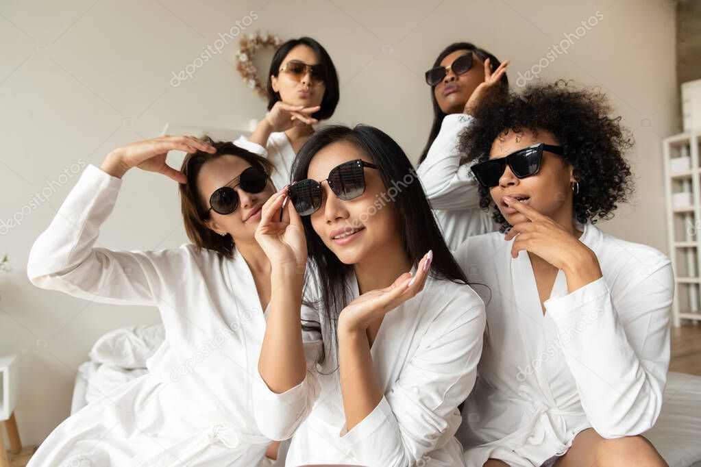 Portrait cool diverse girls wearing sunglasses and bathrobes in bedroom