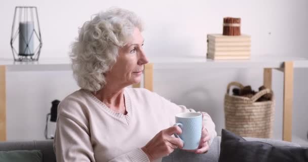Šťastný uvolněný starý žena dívá pryč pití čaje doma — Stock video