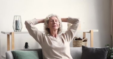 Huzurlu, rahat, yaşlı kadın kanepede, kafasının arkasında dinleniyor.