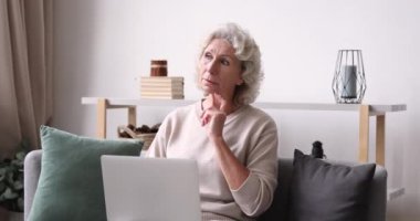 Evde dizüstü bilgisayarda yazan düşünceli yaşlı kadın.