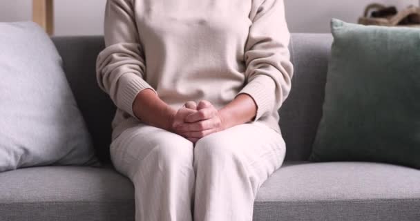 放棄された孤独な年上の女性座っていますソファに手を折り畳む — ストック動画
