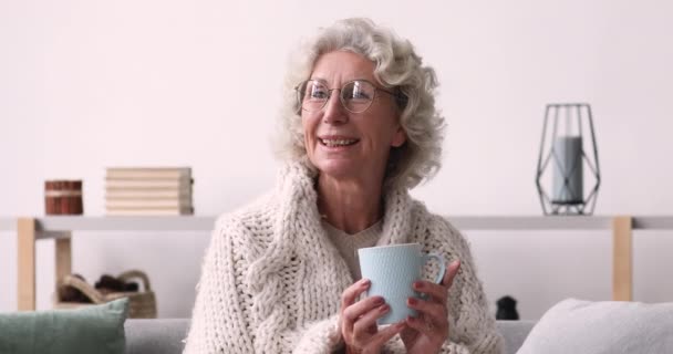 Glimlachende oude vrouw kijken naar camera drinken thee thuis — Stockvideo