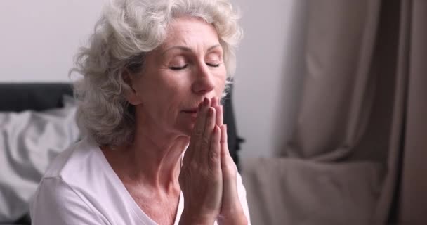 Oudere vrouw biddend met gesloten ogen in slaapkamer, close up — Stockvideo