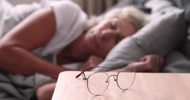 Seniorin wacht morgens mit Brille auf — Stockvideo