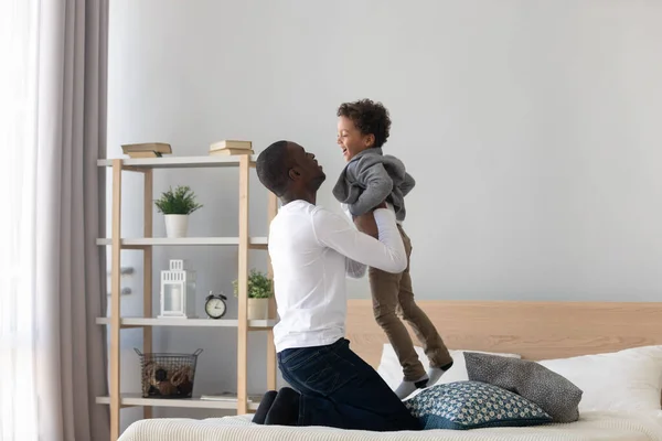 Amoroso padre afroamericano jugando con su pequeño hijo en el dormitorio —  Fotos de Stock