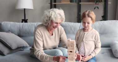 Carefree elderly grandma and small granddaughter playing jenga at home