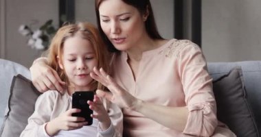 Cute kid daughter having fun with mom using smart phone
