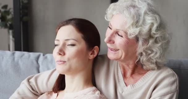 Розслаблена старша мати обіймає молоду дочку і розмовляє на дивані — стокове відео