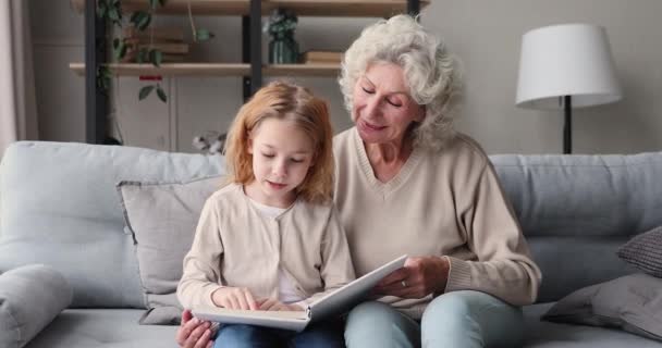 Smart girl granddaughter learning reading with old grandma at home — Stockvideo