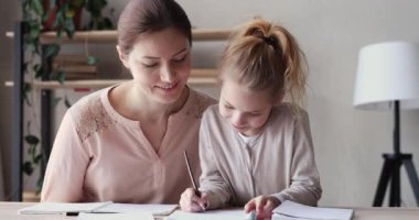 Happy young mum helping cute school child daughter doing homework