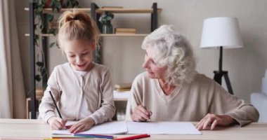 Happy grandmother helping school child granddaughter drawing together