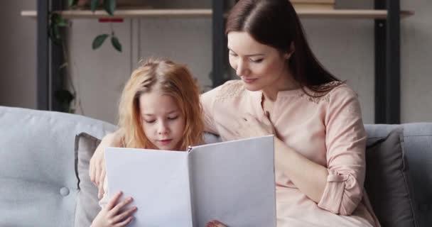 Cute school girl reading book sitting on sofa with mom — Stock video