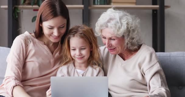 Три поколения женщин семьи смеются, смотря смешные видео на ноутбуке — стоковое видео