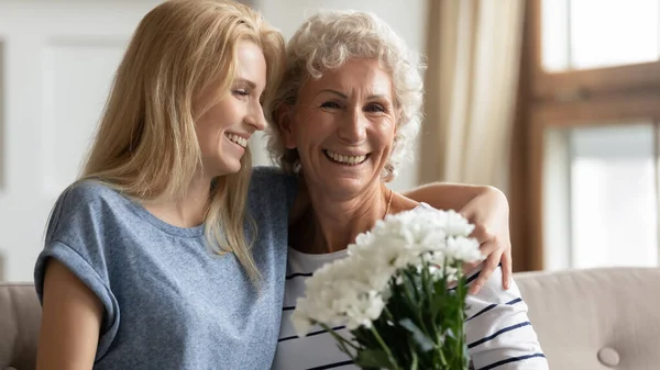 Grownup daughter congratulate mature mom with flowers — Stock Photo, Image