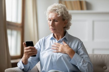 Endişeli olgun kadın cep telefonundaki kötü haberlerden rahatsız oluyor.