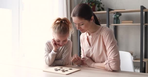 Small daughter and young mom playing checkers at home table — ストック動画