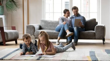 Ebeveynler dijital tablet kullanırken küçük çocuklar resim çiziyor.