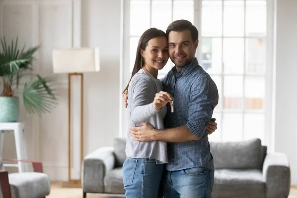 Mutlu genç aile çifti kucaklaşıyor, kameranın anahtarlarını gösteriyor. — Stok fotoğraf