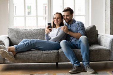 Mutlu genç çift koltukta dinleniyor, cep telefonu ekranına bakıyor..