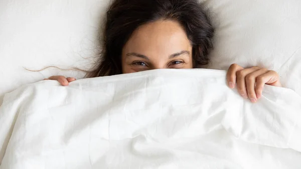 Tersenyum wanita muda bersembunyi di bawah selimut bangun — Stok Foto