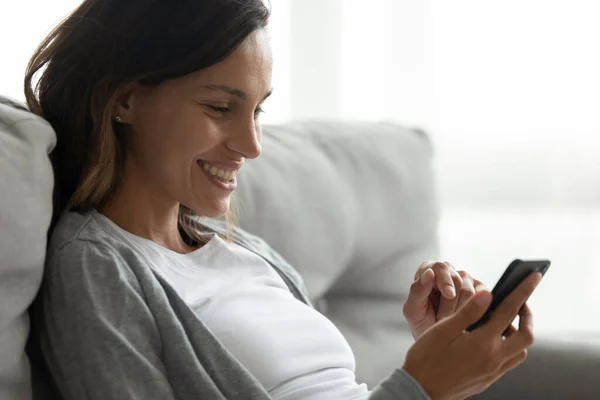 Mujer joven feliz sentarse en el sofá utilizando Internet en el teléfono inteligente — Foto de Stock