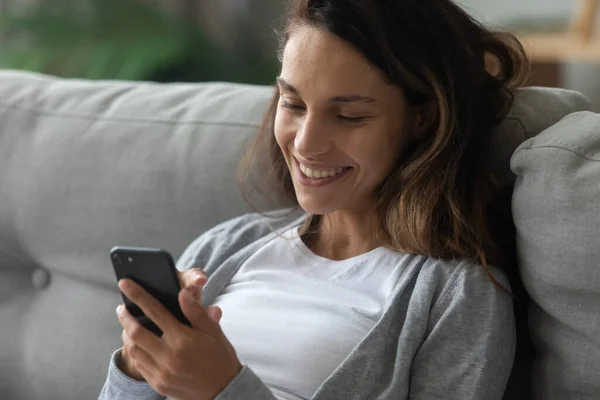 Happy millennial girl relax on couch using cell phone — стоковое фото