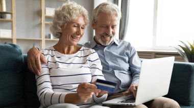 Gülümseyen yaşlı çift evde online alışveriş yapıyor.